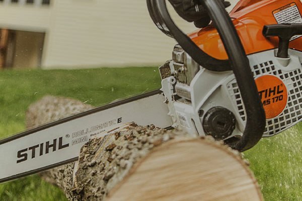 Gas chainsaw cutting through a log on a lawn